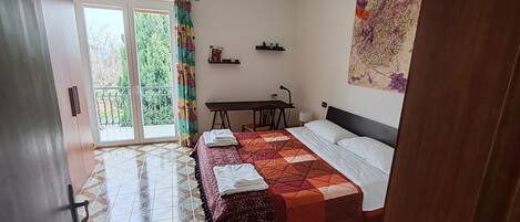 Un dormitorio con una cama, un escritorio y una silla. Hay una ventana con cortina, un estante en la pared y un cuadro.