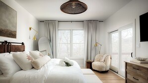 Une chambre moderne avec un grand lit, une chaise, une commode en bois et une grande fenêtre.