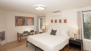 Une chambre à coucher comprenant un lit, des tables de chevet, un bureau, des chaises et des œuvres d’art accrochées aux murs.