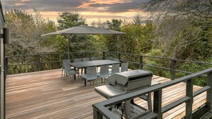 Une terrasse extérieure avec une table et des chaises, un barbecue et une vue sur les arbres et le ciel.
