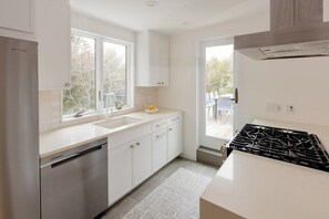 Una cocina moderna con armarios blancos, un refrigerador de acero inoxidable, una estufa a gas y un ventanal que proporciona luz natural.