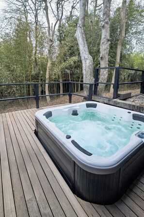 Un bain à remous sur une terrasse en bois, entouré d’arbres.