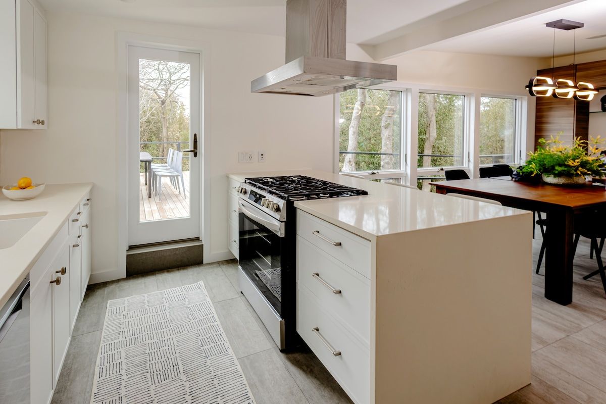 Een moderne keuken met een centraal eiland, een fornuis en een eethoek met een tafel en stoelen.