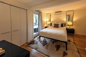 Une chambre à coucher comprenant un lit, des tables de chevet, une armoire et une porte donnant sur un balcon.