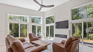 A spacious living room with large windows, a fireplace, and leather furniture. - Summer Breeze at Goose Rocks Beach (Kennebunkport)