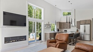 A modern kitchen with a dining area, a fireplace, and a large window overlooking greenery. - Summer Breeze at Goose Rocks Beach (Kennebunkport)