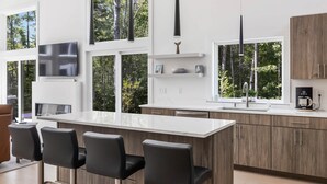 A modern kitchen with a large island, bar stools, a flat-screen TV, and a coffee maker. - Summer Breeze at Goose Rocks Beach (Kennebunkport)