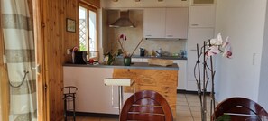 Een keuken met houten kastjes, een centraal eiland en een zithoek met twee stoelen.