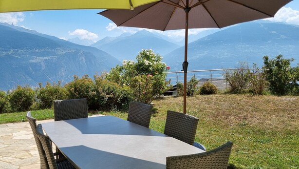 Een terras met een tafel en stoelen, omgeven door groen en een uitzicht op een berg.