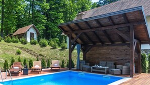 A swimming pool with wooden deck seating and a covered area with wicker furniture.