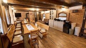 A rustic dining area with wooden furniture, a long table, and benches. There is a kitchen area with a coffee machine and cabinets.