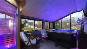 A spa room with a massage table, a chair, and a large window offering a view of the outdoors.