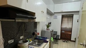Cozinha compacta com armários brancos, fogão e pia. Há um pequeno espaço de refeições com mesa e cadeiras.
