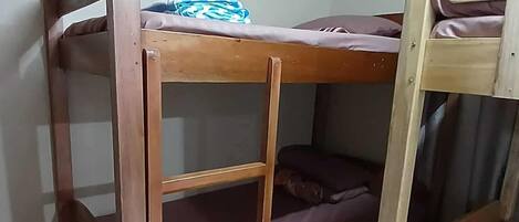 A bunk bed room with a wooden frame, a lower bunk with a striped pillow, and a top bunk with a blue and white pillow.