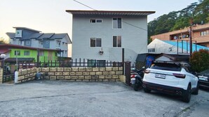 A residential area with a two-story house, a fenced yard, a parked white car, and a motorcycle. - Budget Accommodation near Town (Campo Sioco Baguio City)
