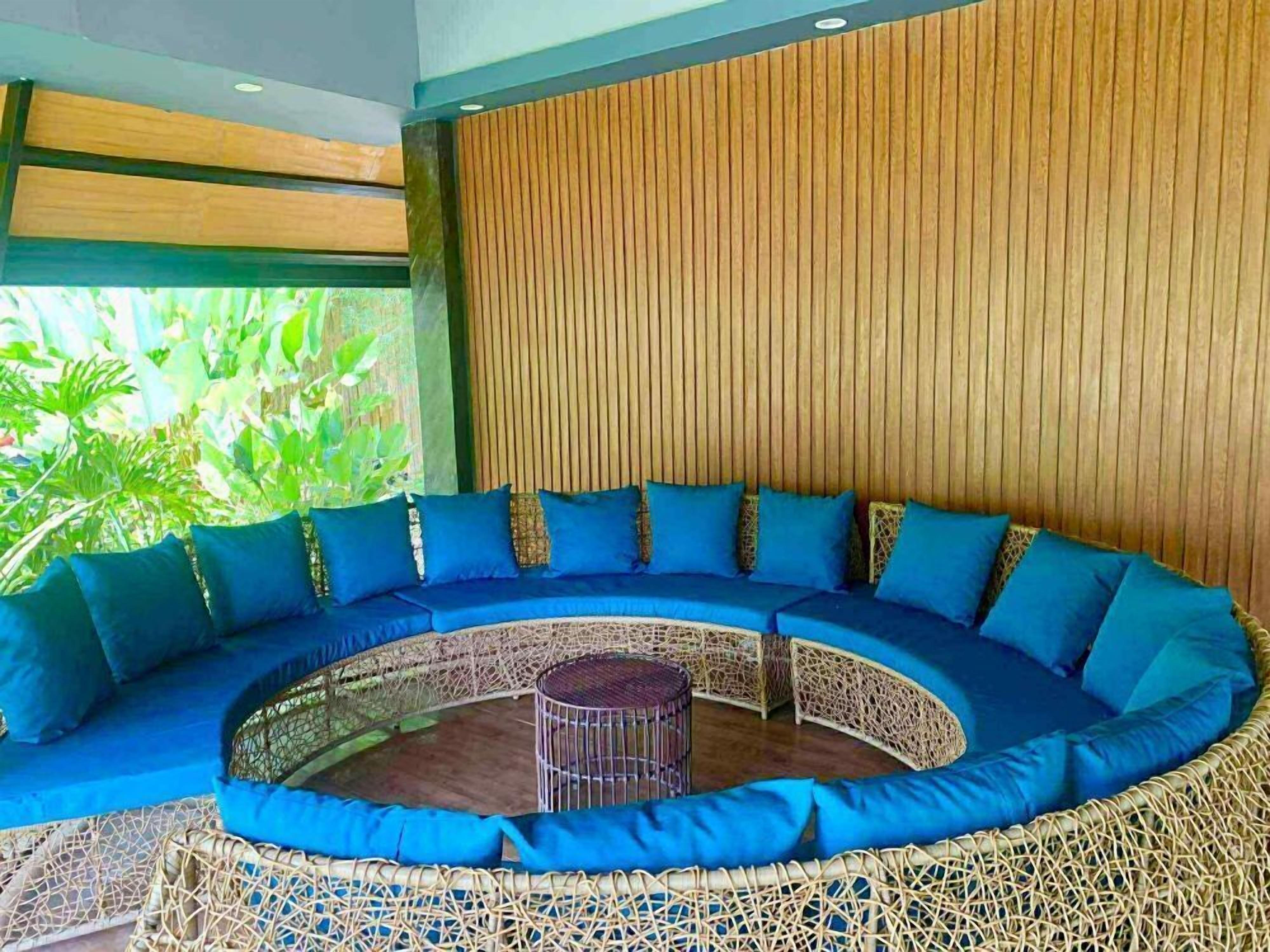 A circular outdoor seating area with blue cushions and a central round table, surrounded by a woven fence.