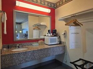 A hotel bathroom with a granite countertop, a sink, a mirror, a towel rack, a hairdryer, and a coffee maker. - Winnie Inn Suites & RV Park (Winnie)