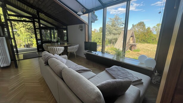 A modern living room with a large sofa, a dining table, and a TV. - Vacation home-Nature-Elbe-View-Fully equipped (Magdeburg)