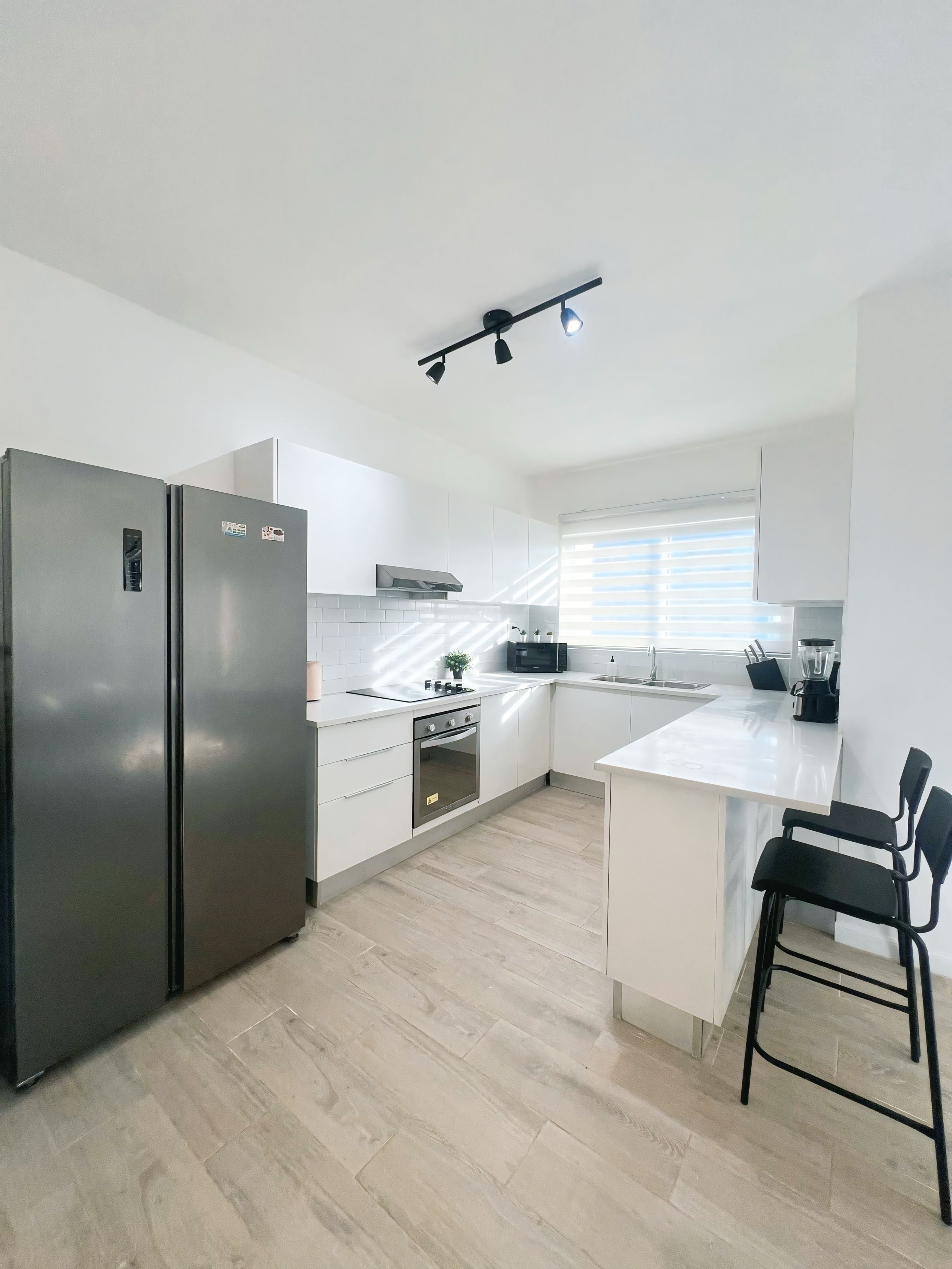 A modern kitchen with white cabinets, a stainless steel refrigerator, a built-in oven, and a black countertop.