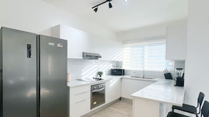 Cozinha moderna com armários brancos, geladeira de aço inoxidável, forno embutido e bancada preta.