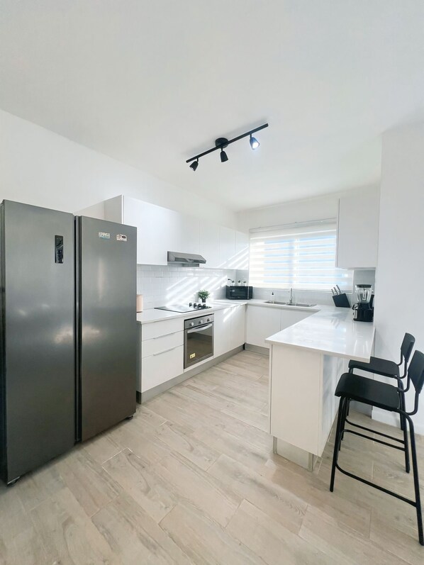 A modern kitchen with white cabinets, a stainless steel refrigerator, a built-in oven, and a black countertop.
