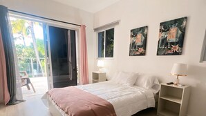 Um quarto com cama, ventilador de teto, mesa de cabeceira e janela.