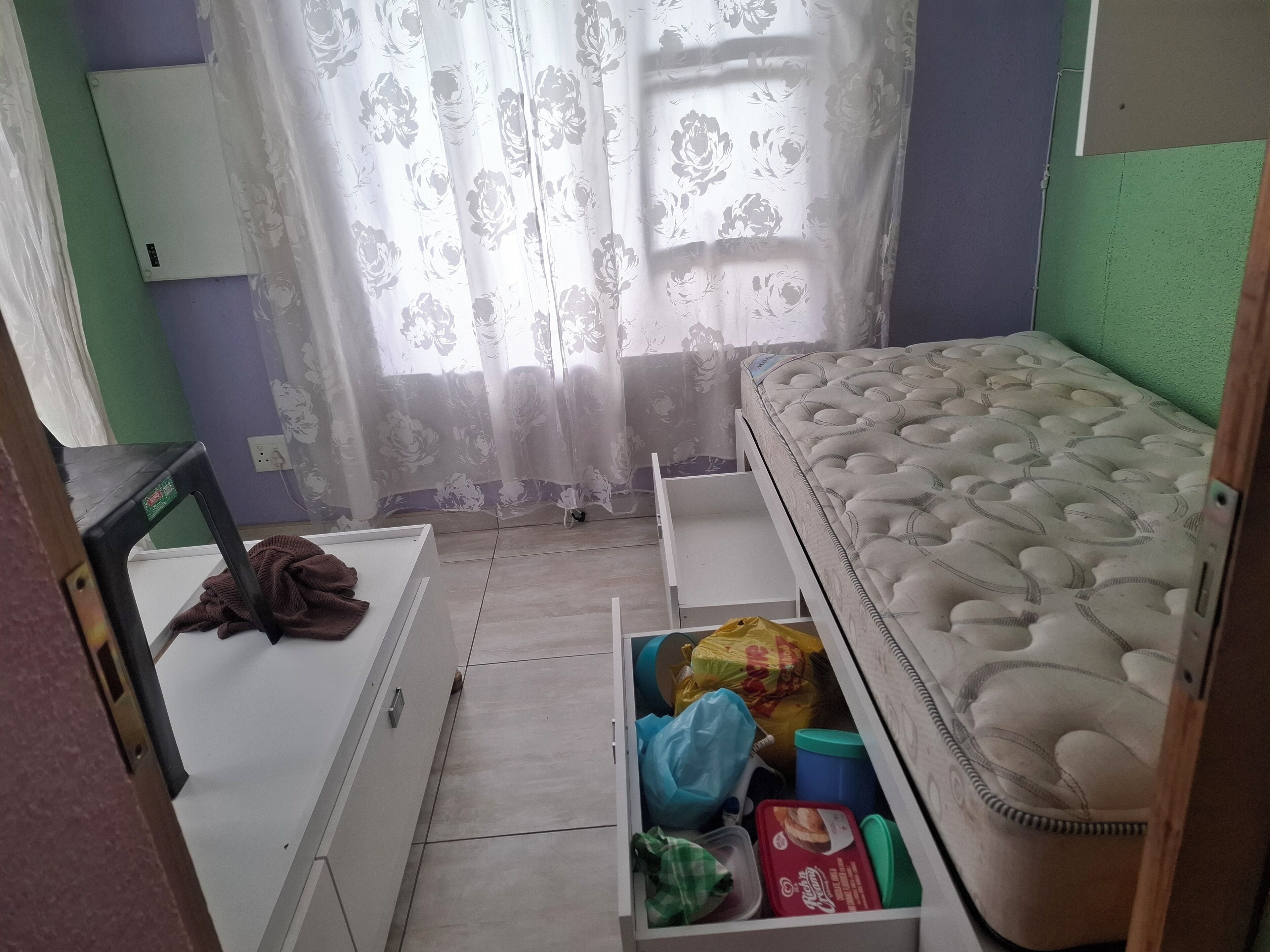 A small, compact room with a bed, a chair, a desk, and a storage unit.