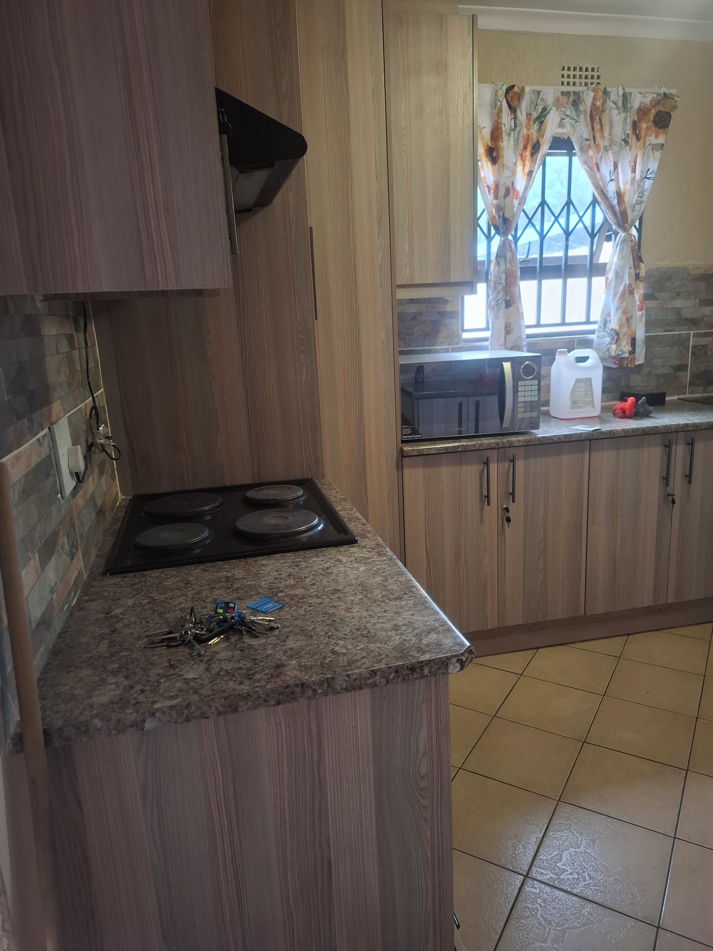 Une cuisine avec des meubles en bois, un plan de travail en granit, une cuisinière, un four à micro-ondes et une fenêtre agrémentée de rideaux à motifs floraux.