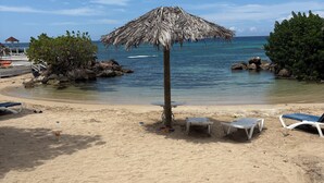 A beach with a thatched umbrella, lounge chairs, and rocky outcrops in the water. - Runaway Bay Caldo Tours (Runaway Bay)
