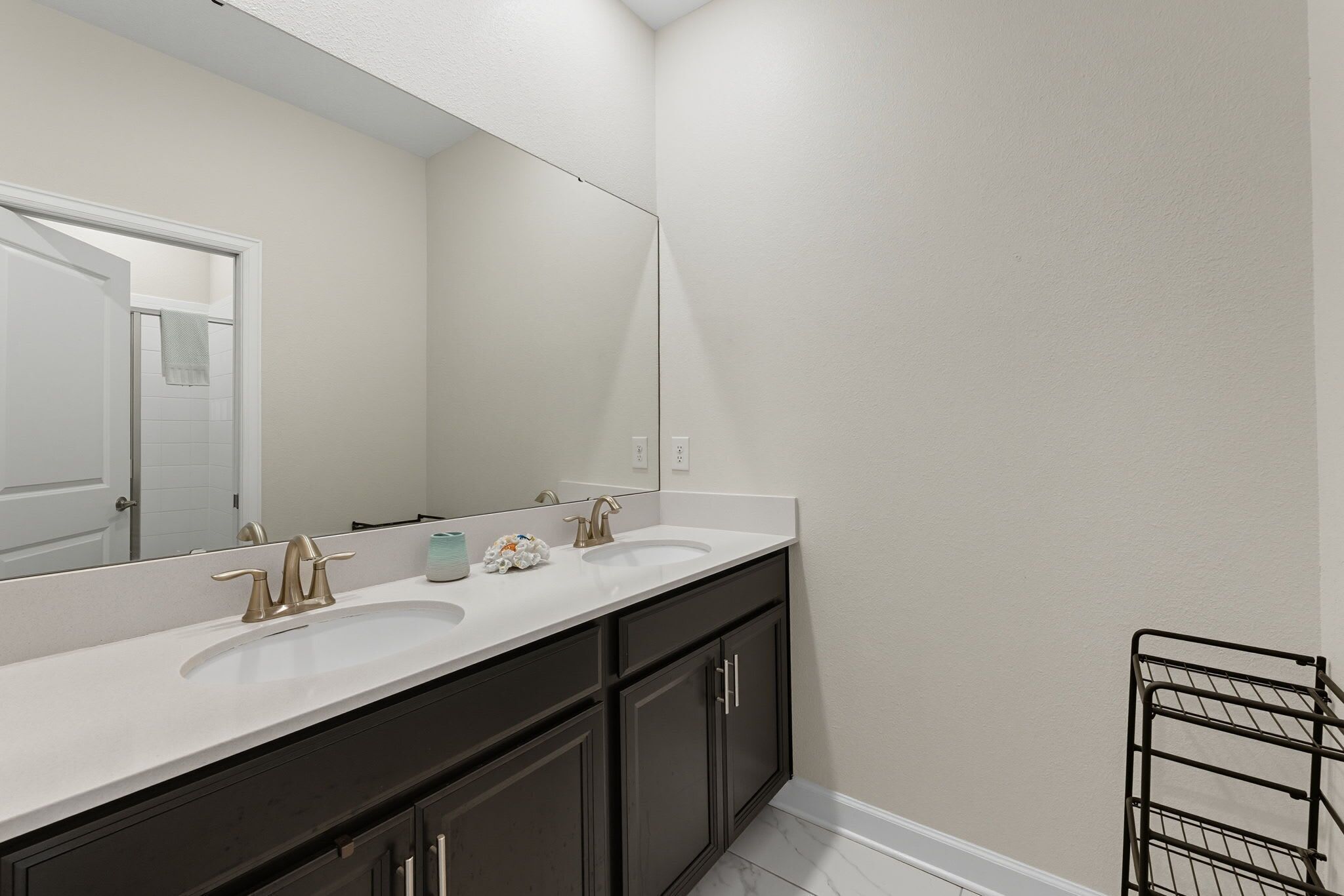 A bathroom with two sinks, a large mirror, dark cabinets, and a towel rack.