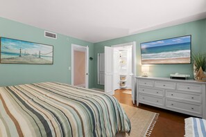 A bedroom with a bed, a dresser, a painting of a beach, and a door leading to a closet. - Shorehom by the Sea 75 (New Smyrna Beach)