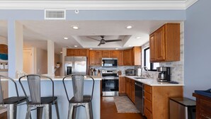 A modern kitchen with wooden cabinets, stainless steel appliances, and a central island with bar stools. - Shorehom by the Sea 75 (New Smyrna Beach)