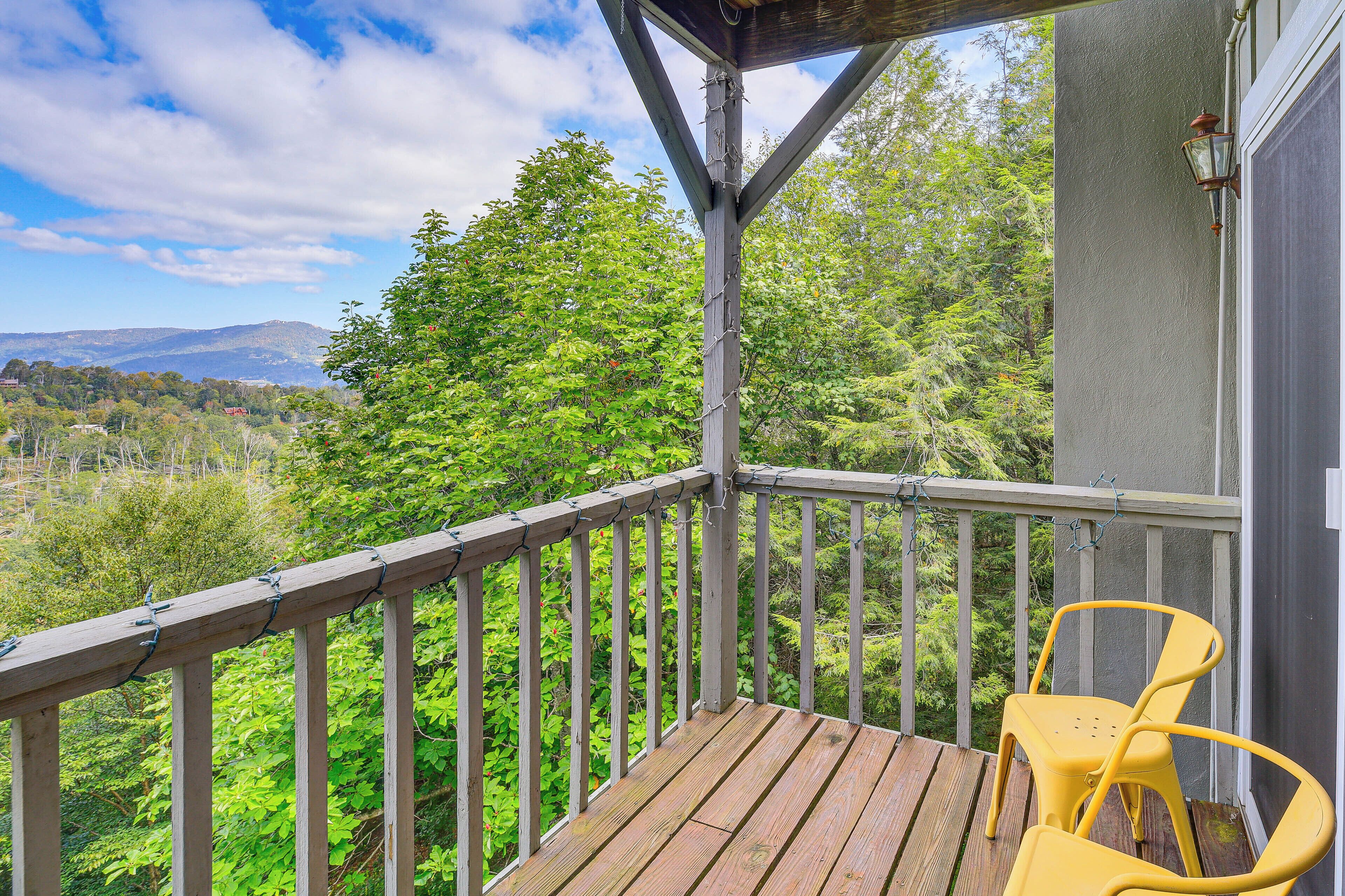 A wooden deck with a railing, a yellow chair, and a view of a forested area with mountains in the distance.