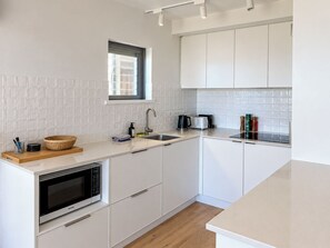 Une cuisine moderne avec des meubles blancs, un four à micro-ondes encastré, un évier et une fenêtre.