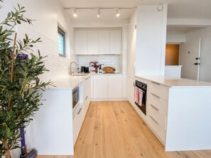 A modern kitchen with white cabinetry, a wooden floor, and a built-in oven. - Shoreline Retreat - beach frontage - 2 King Beds (Scarborough)