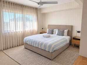 A bedroom with a bed, curtains, a ceiling fan, and a nightstand.