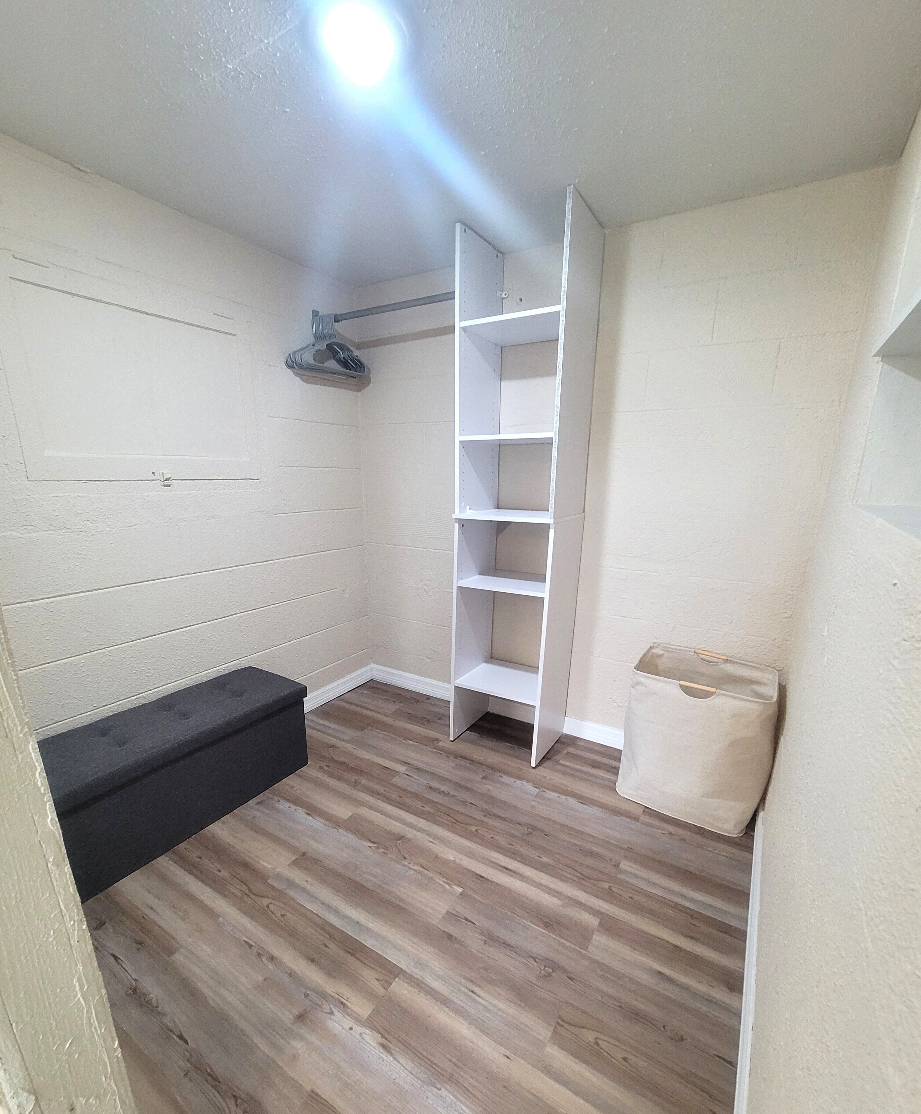 Ein Zimmer mit Holzboden, einer schwarzen Bank, einer weißen Wand und einem weißen Regal.