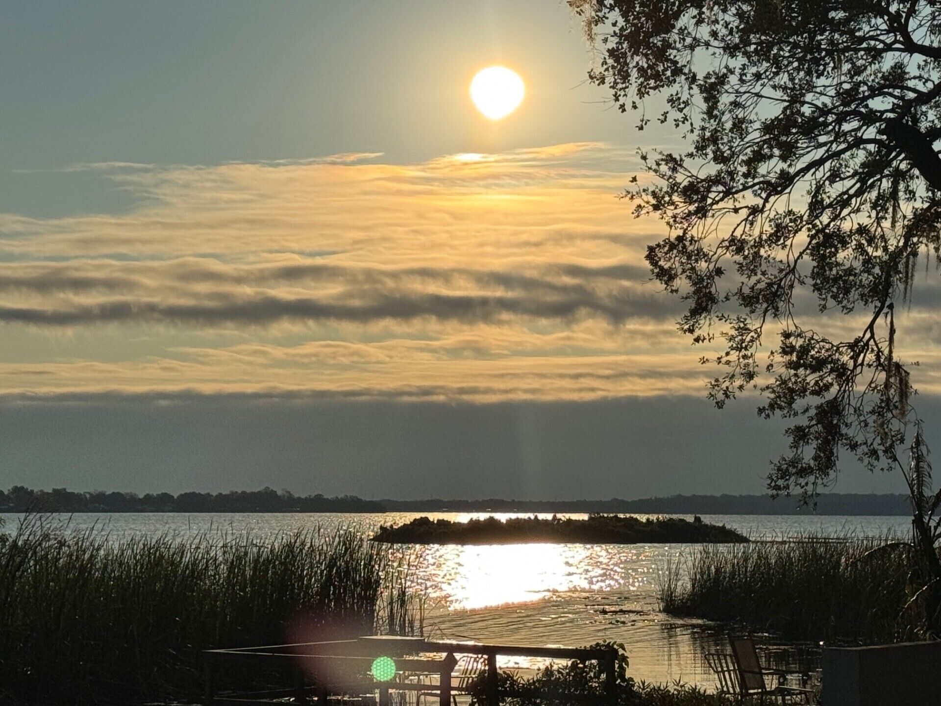 A sunset over a body of water with a dock and chairs.