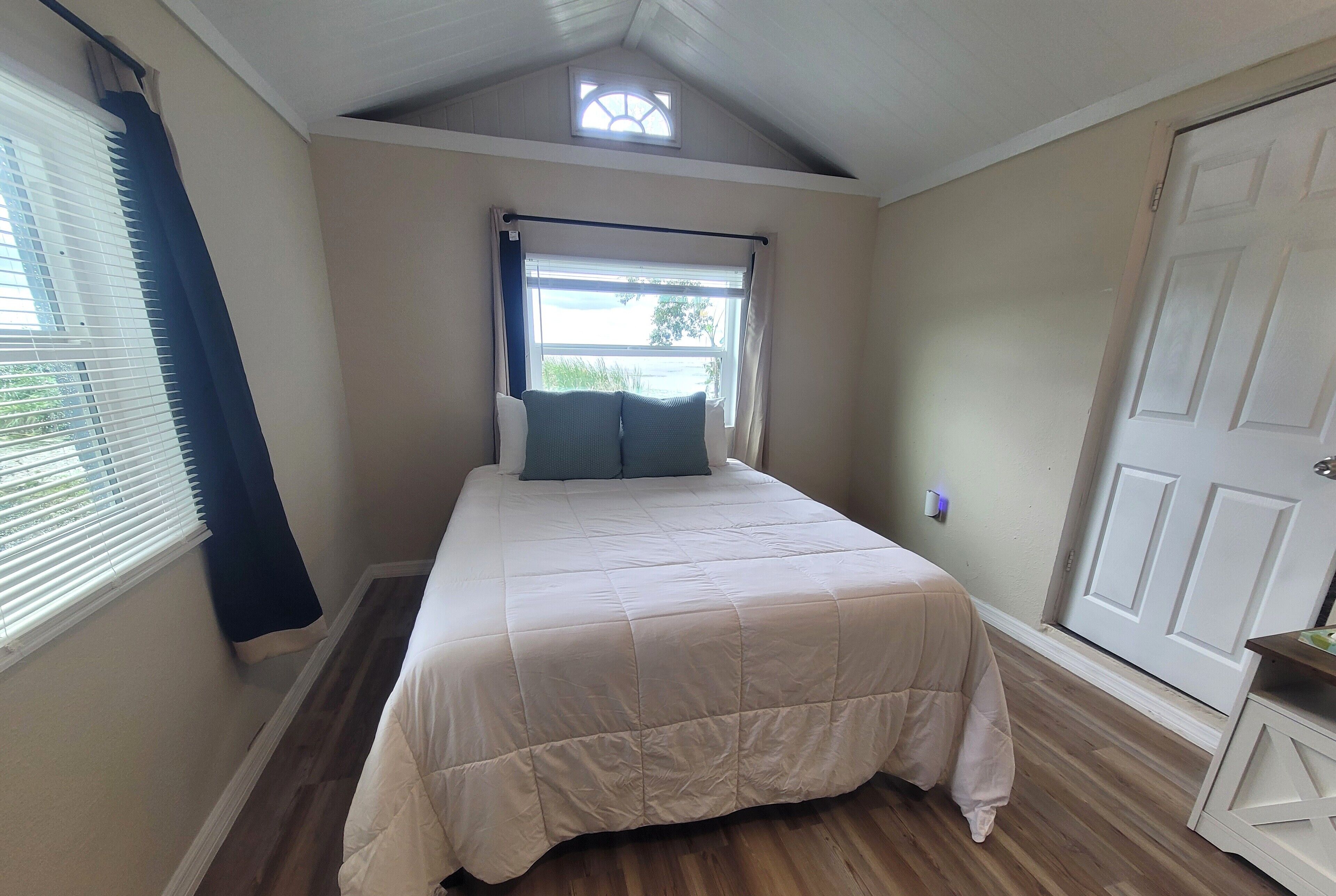 Une chambre à coucher avec un lit, une fenêtre avec des rideaux, une porte et une petite lucarne.