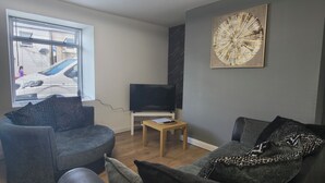 A modern living room with a grey sofa, a black leather armchair, and a wooden coffee table. A flat-screen TV is on a stand, and a large abstract painting is on the wall. - Hetton Modern Stay near Durham (Hetton-le-Hole)