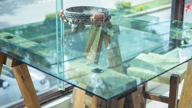 Una mesa con cubierta de vidrio, un cuenco decorativo y patas de madera.