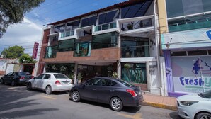 Un edificio de varios pisos con un letrero de hotel, coches estacionados y una tienda con el rótulo 'Freshy'.