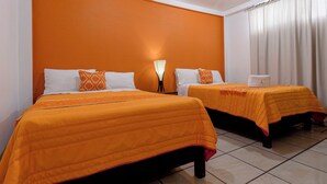 Habitación de hotel con dos camas, ropa de cama naranja, almohadas blancas y un ventanal con cortinas.