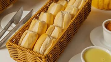 A wicker basket filled with bread rolls, a white plate, a knife, and a bowl of butter.