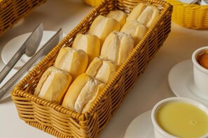 Una cesta de mimbre llena de panecillos, un plato blanco, un cuchillo y un bol de mantequilla.