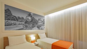 Una habitación de hotel con dos camas, una mesita de noche con lámpara y un cuadro grande en blanco y negro de un tren en la pared.