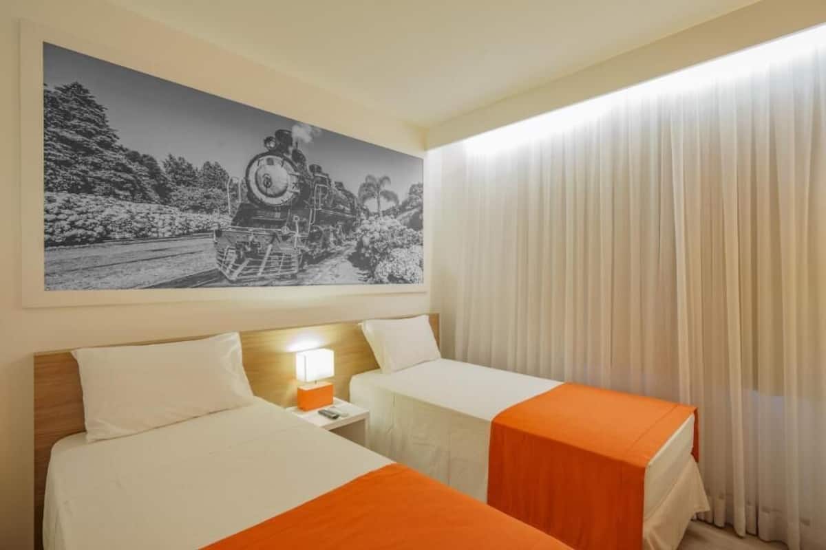 Una habitación de hotel con dos camas, una mesita de noche con lámpara y un cuadro grande en blanco y negro de un tren en la pared.