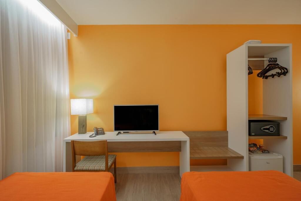 Habitación de hotel con escritorio, televisión, armario y dos camas.