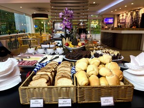Un buffet proposant une variété de plats, notamment du pain, des gâteaux et des fruits.