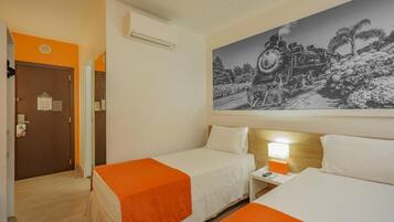 A hotel room with two beds, an orange bedspread, a nightstand with a lamp, and a large black and white photo of a train on the wall.